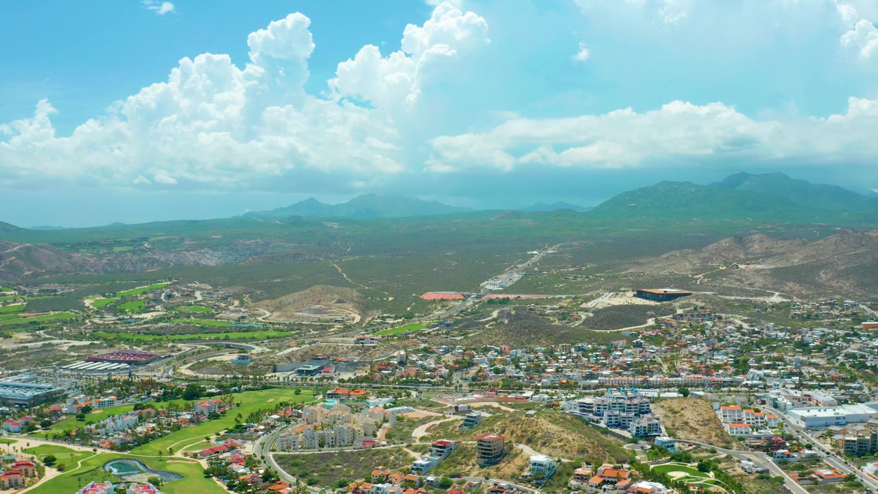 Drone view over a mountainous townscape with fields, roads, hills, and blue sky.