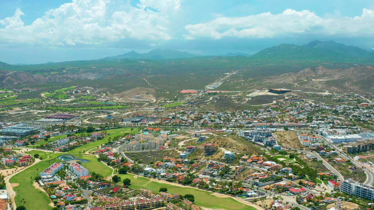 Aerial town view with golf greens, hills, mountains, and bright clouds