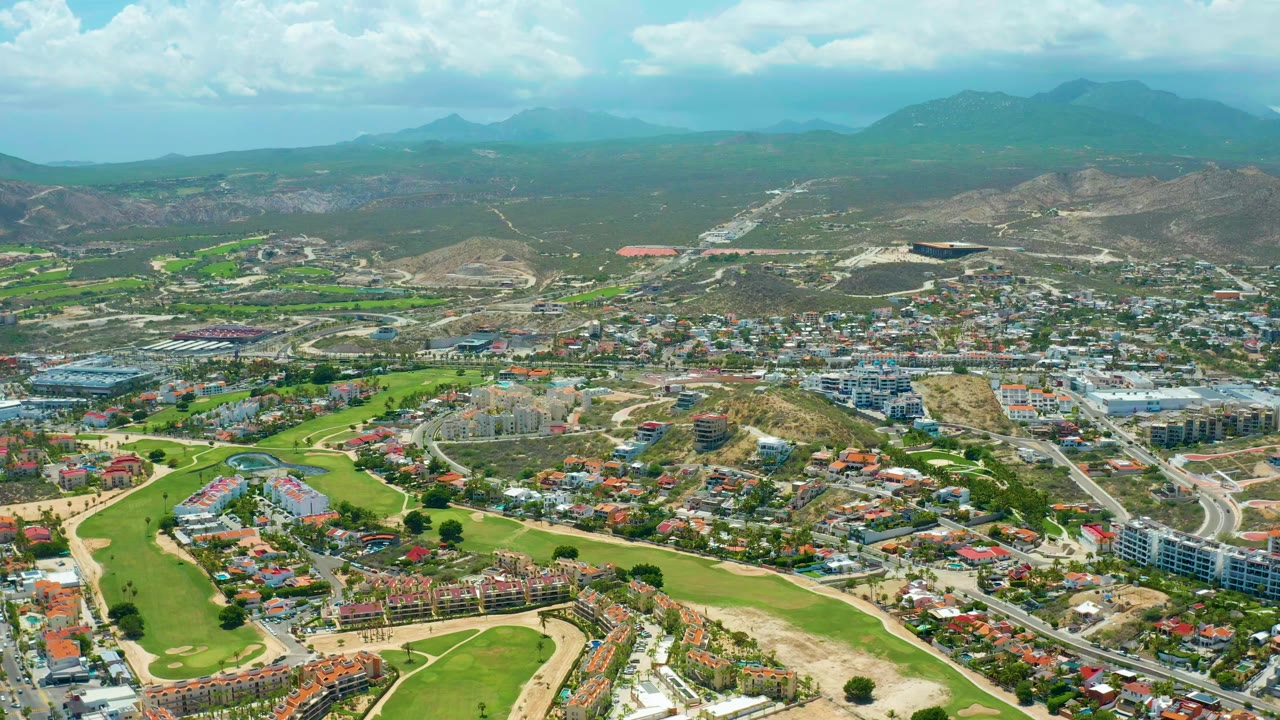 Aerial view across fairways, residential streets, hills, and cloudy sky.