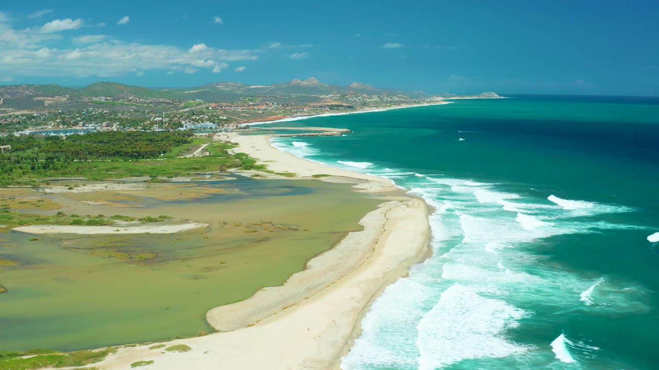 Beach and lagoon viewed from above with ocean surf breaking along the right.
