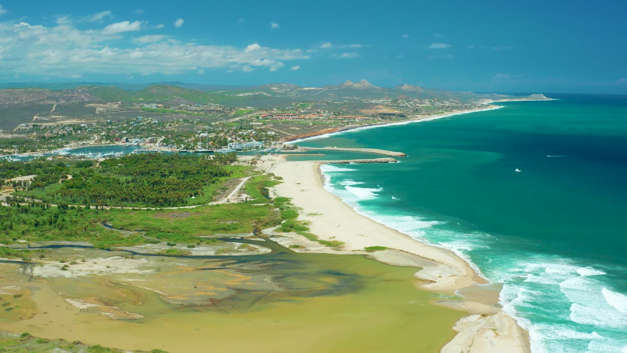 Aerial view of lagoon, beach, ocean surf, vegetation, town, and hills.