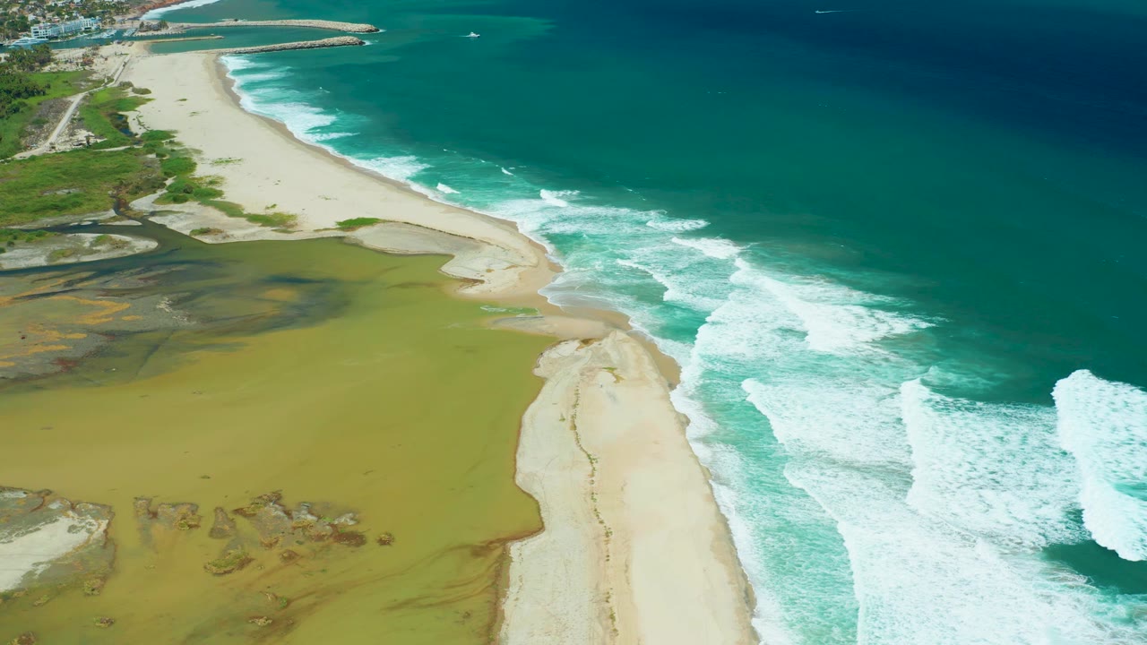 High aerial of a beach between green lagoon water and blue ocean.