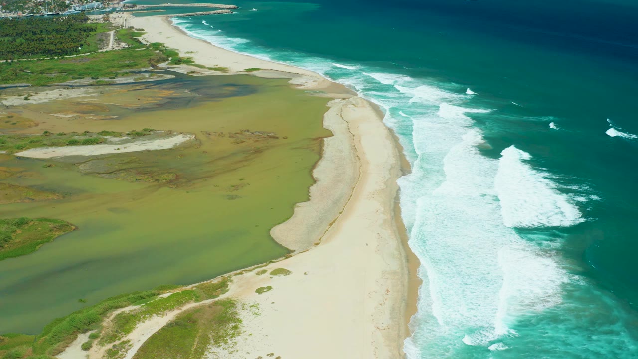 High aerial beach scene with marsh water and waves rolling in.