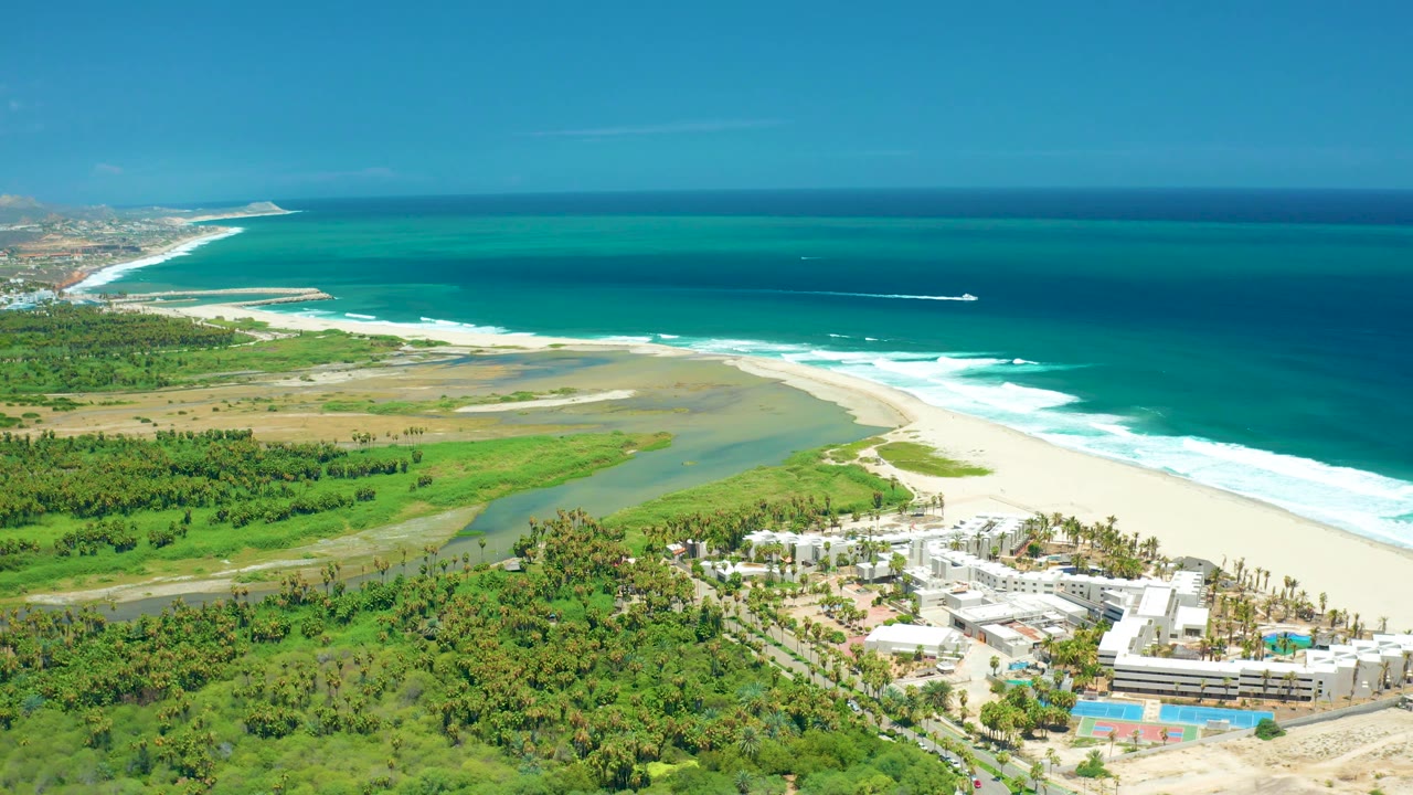 Coastline aerial with boat offshore and white surf along a long beach.