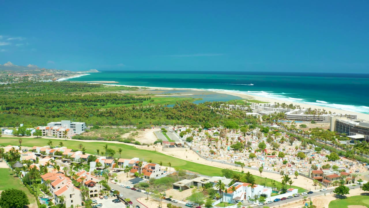 Drone-height coastline view with beach umbrellas, resort buildings, and ocean.