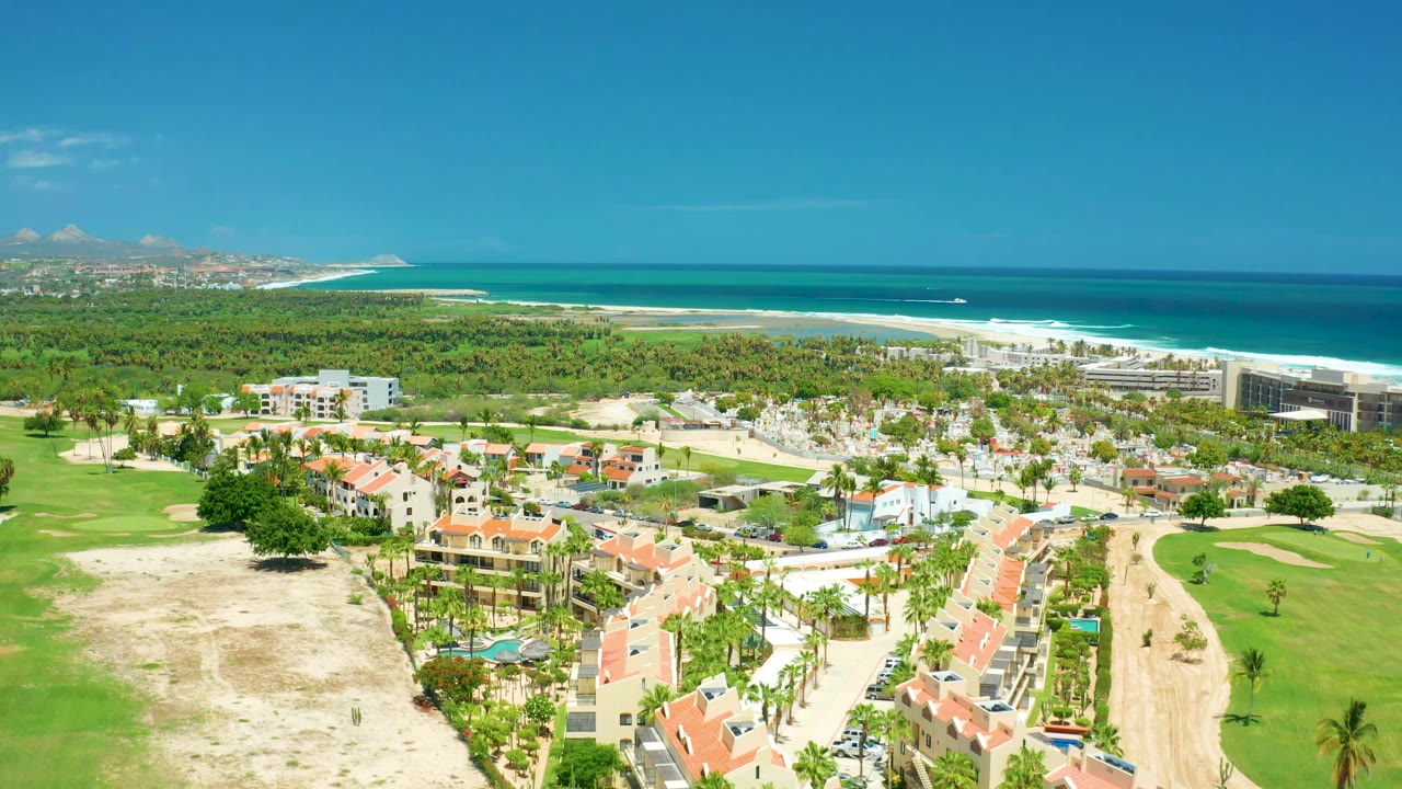Wide drone view of beachfront development, golf course, red roofs, and ocean.