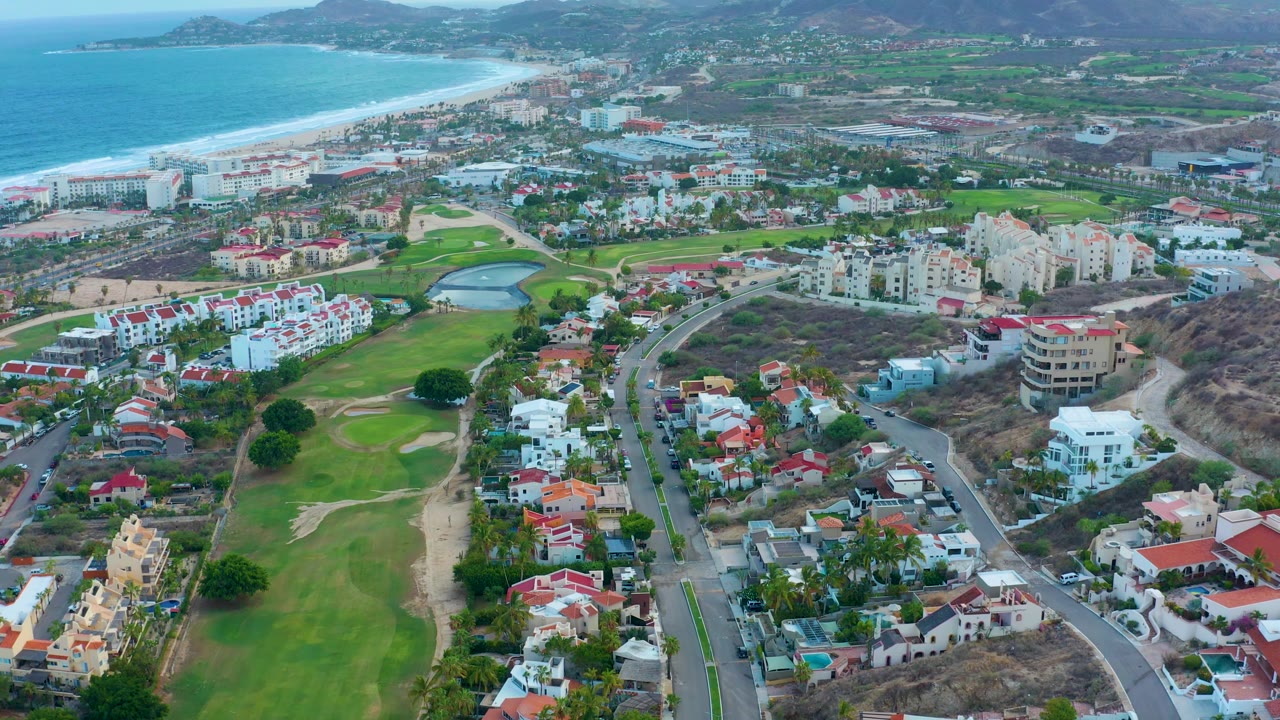 Aerial coastal town view with golf course, homes, roadway, beach, and sea.