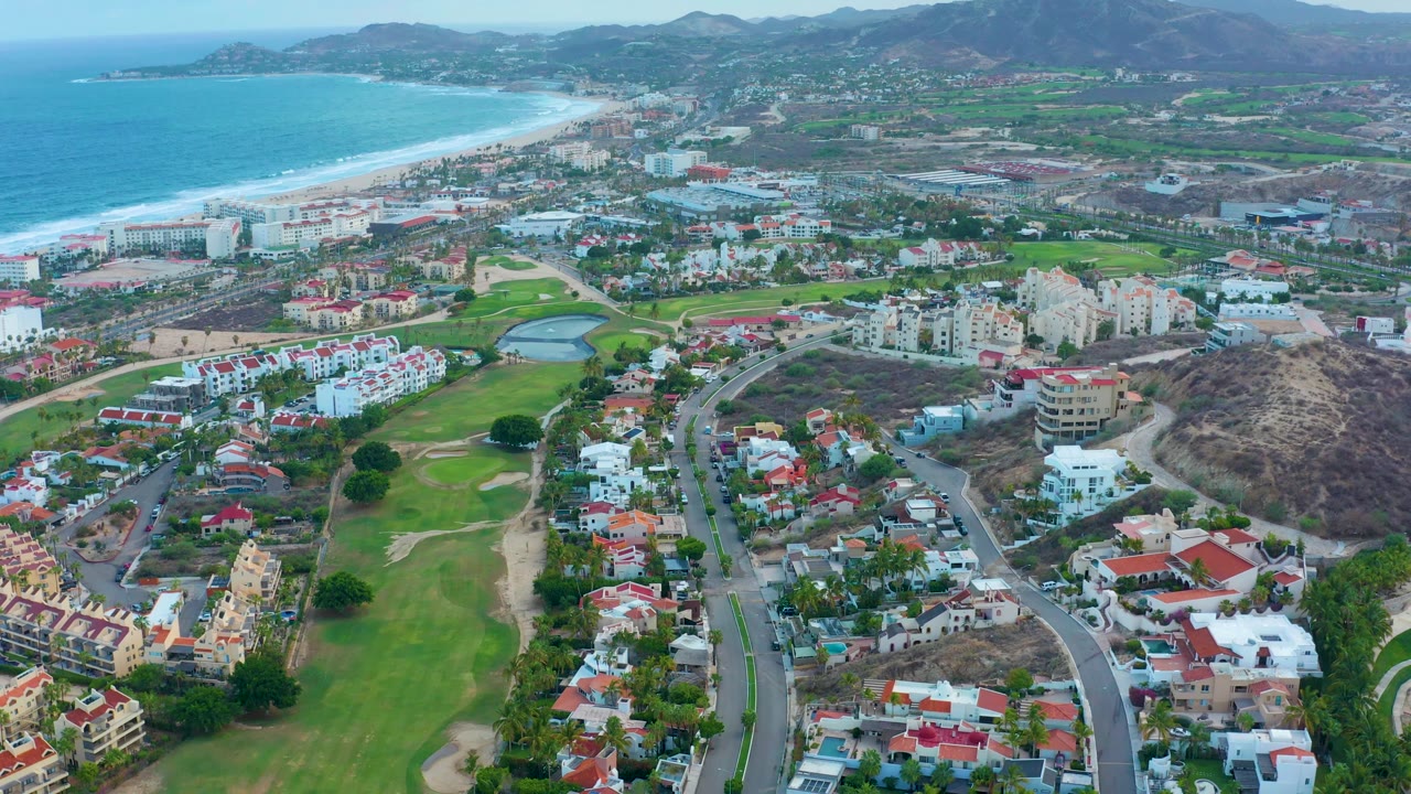 Drone view looking across golf fairways, roads, homes, beach, and ocean.