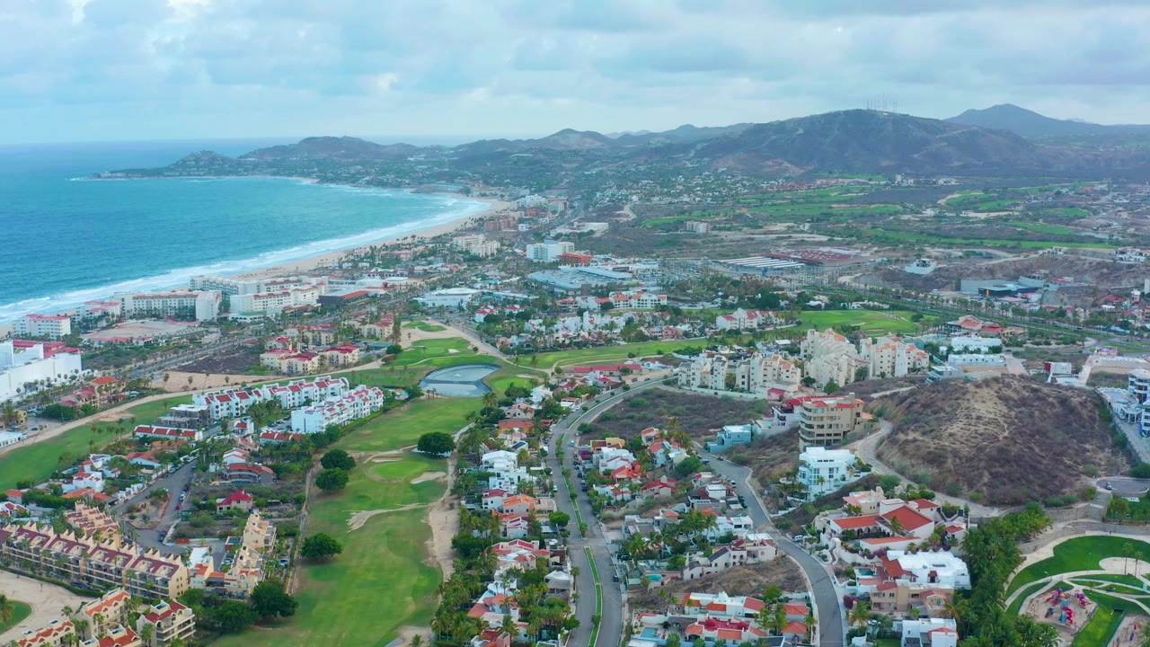High view of beach, resort area, golf course, roads, and hills.