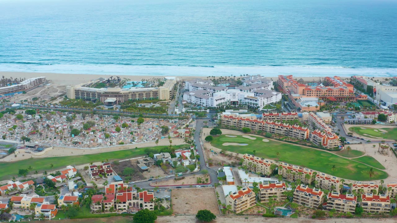 Aerial view of beach umbrellas, resort buildings, and ocean surf.
