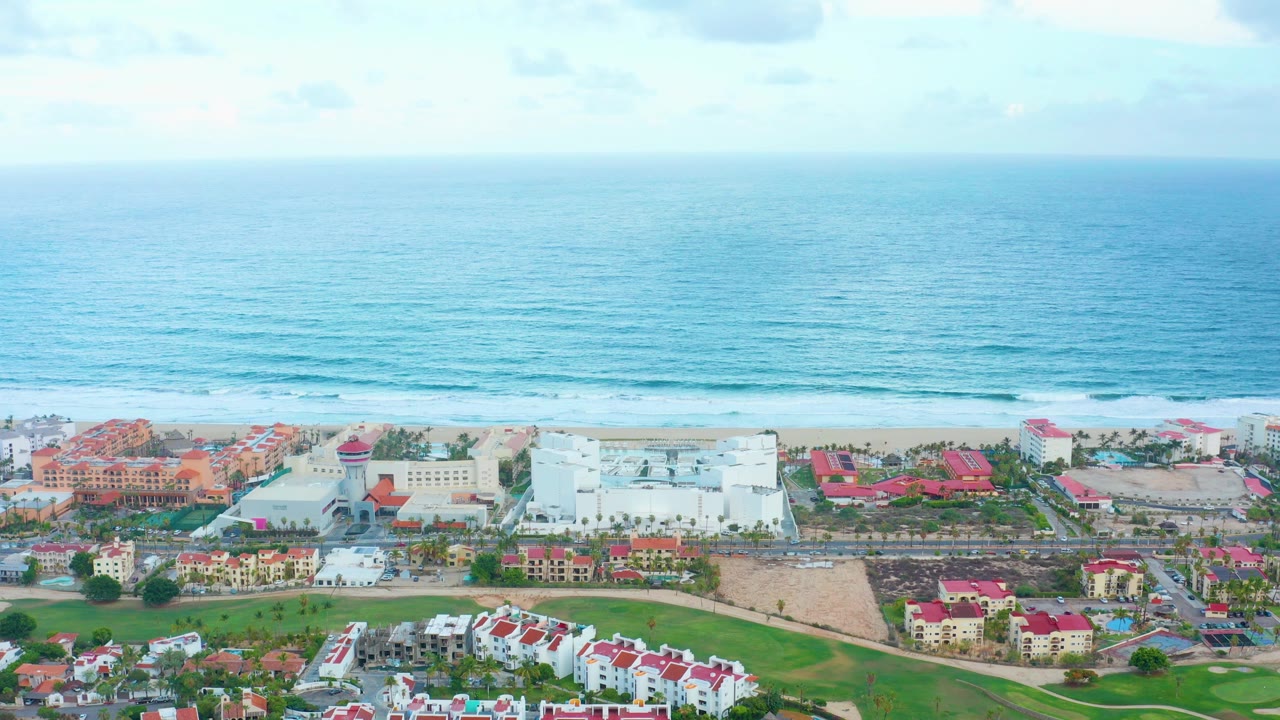Aerial shoreline view with resort rooftops, beach, waves, and sky.