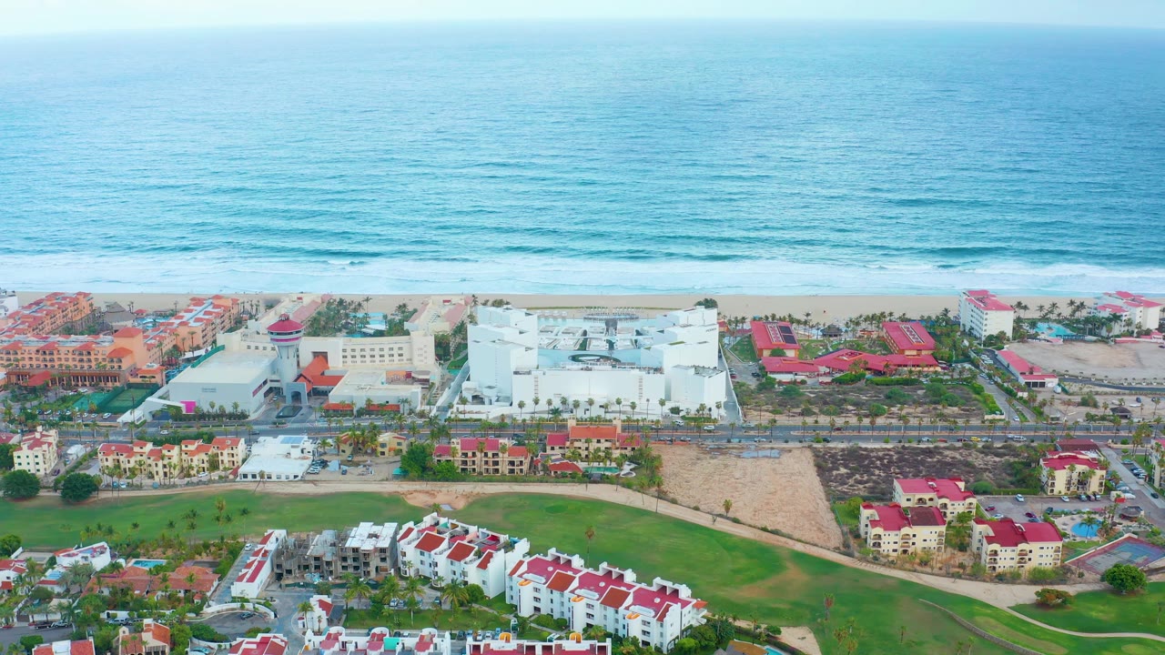 Wide drone-like view of beach resort frontage and ocean waves.