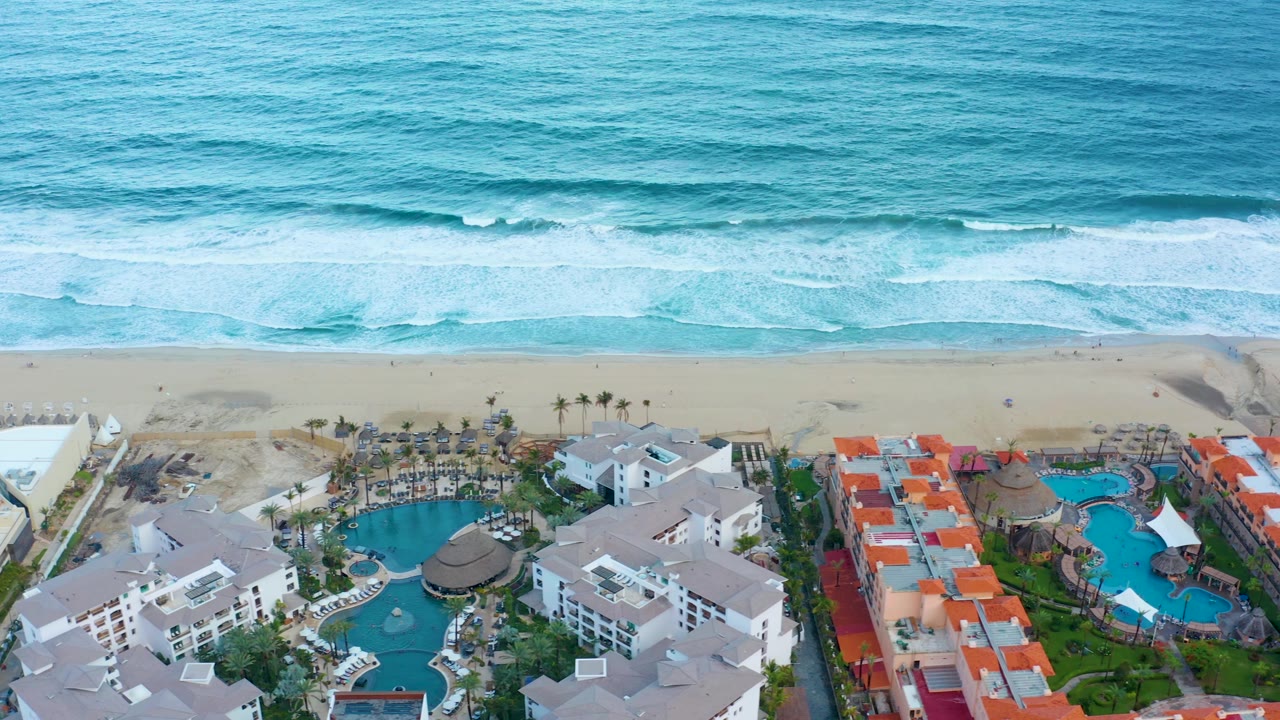 Drone view of resort pools beside beach and rolling ocean waves