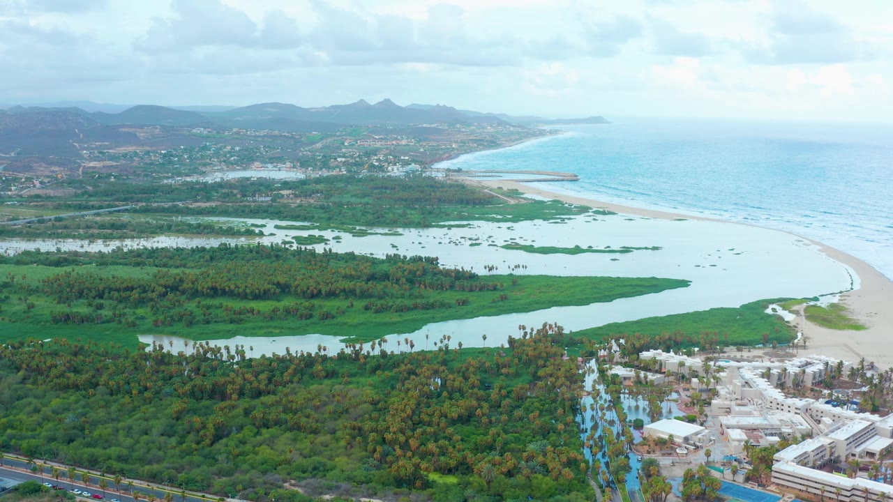 Aerial coastline with lagoon, greenery, beach, ocean, and distant mountains.