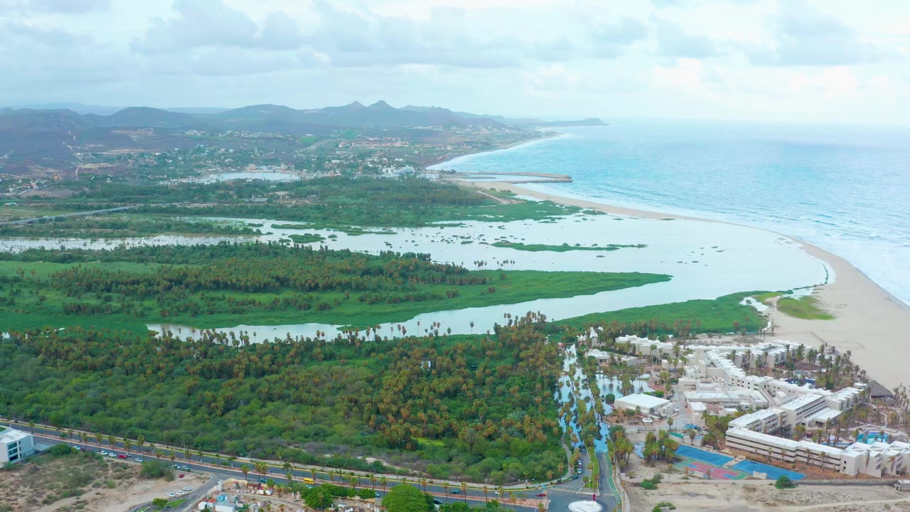 Wide drone view of coastal lagoon and beach beside developed roads.