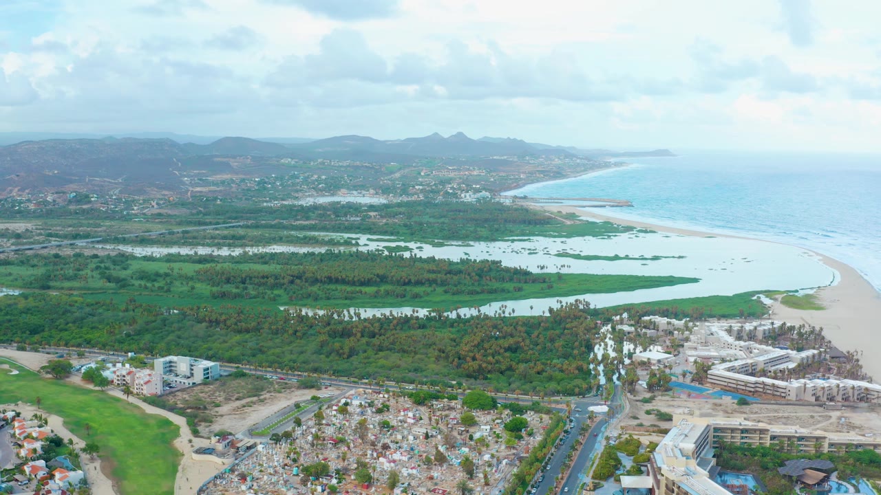 Drone view across town buildings, coastal wetlands, beach, ocean, and distant hills.