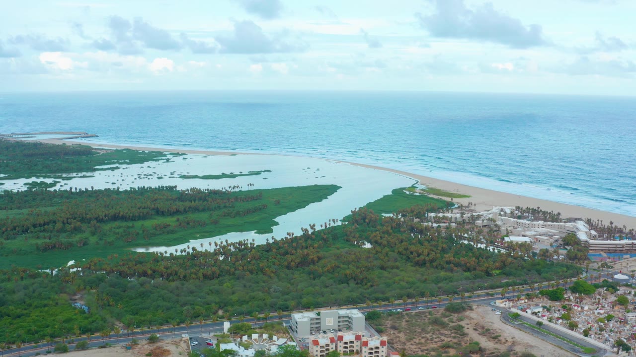 Coastal aerial view with lagoon, beach, ocean, vegetation, and shoreline buildings.