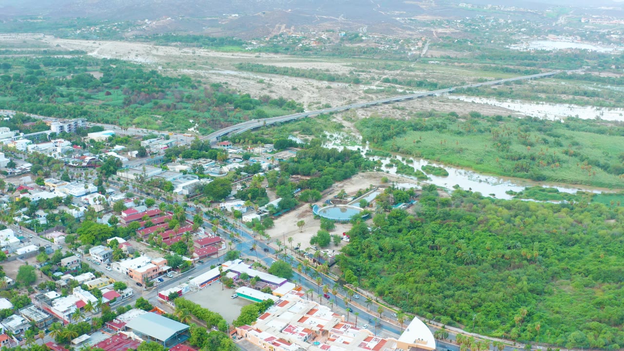 Aerial view across green vegetation, river water, roads, buildings, and hazy mountains.