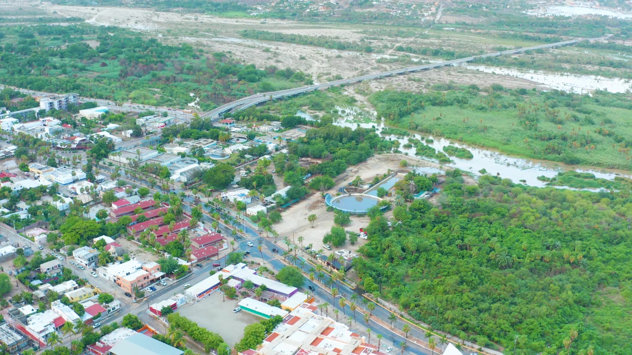 Aerial town-edge scene with flooded waterway, trees, and streets.