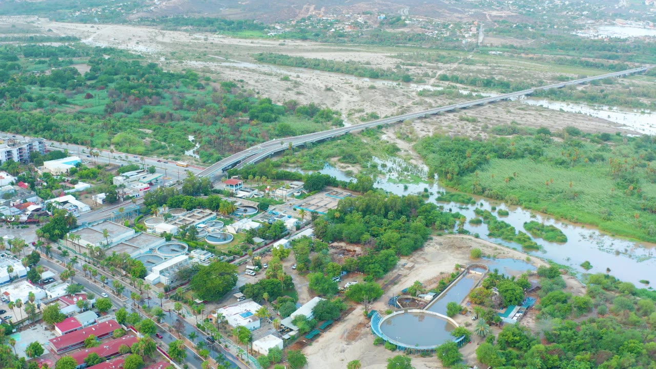 High aerial view of a river channel beside roads, buildings, and circular tanks.