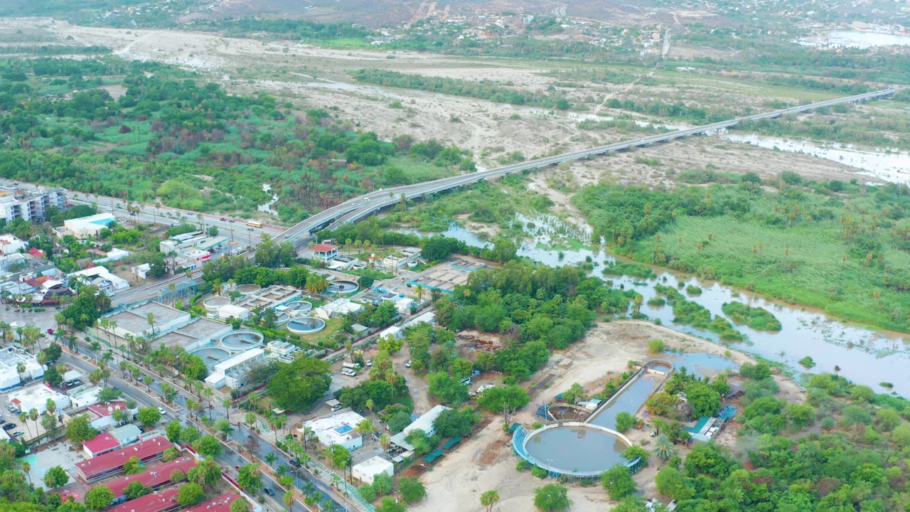 Third frame shows San Jose Del Cabo's green river edge, pale exposed riverbed, road bridge, roadside buildings, and circular tanks, with no visible people.