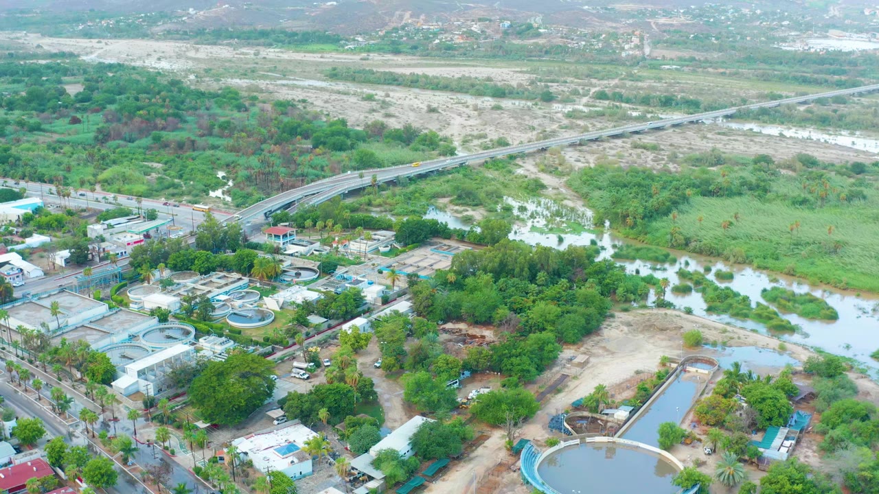 Drone view of a green waterway with bridge, road grid, pools, and buildings.