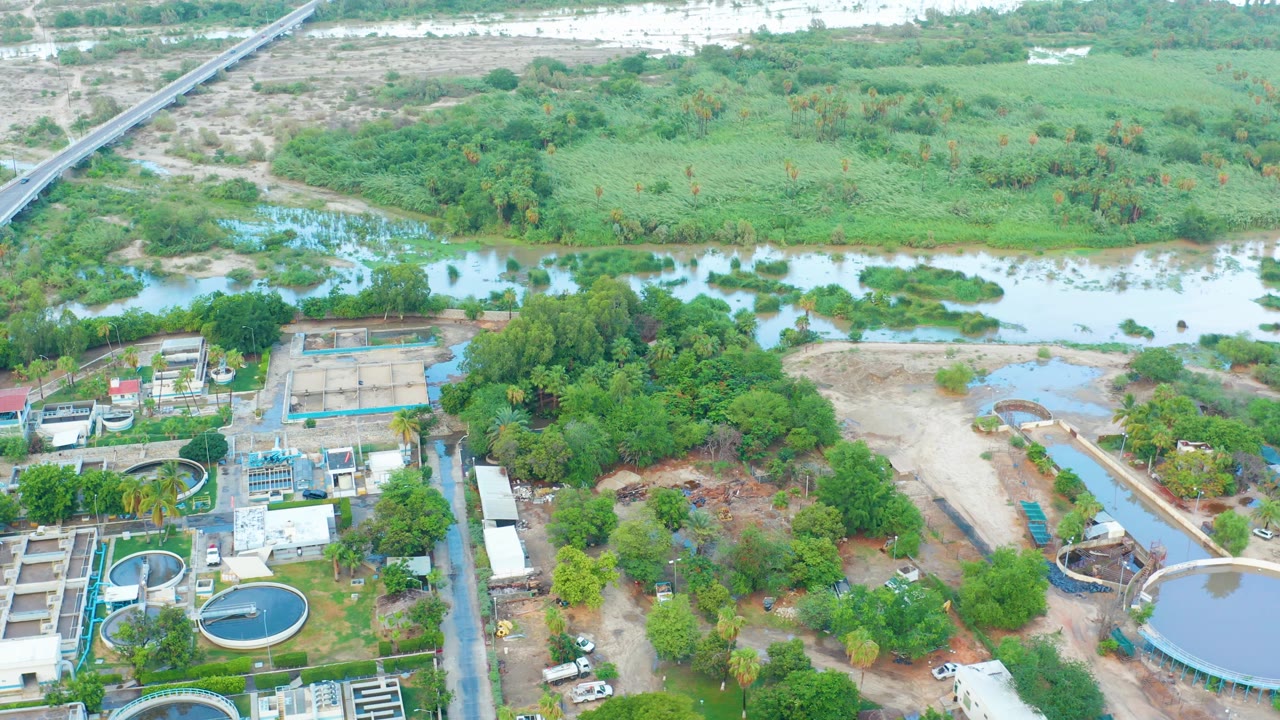 Aerial view of water tanks beside a green river corridor and scrubland.