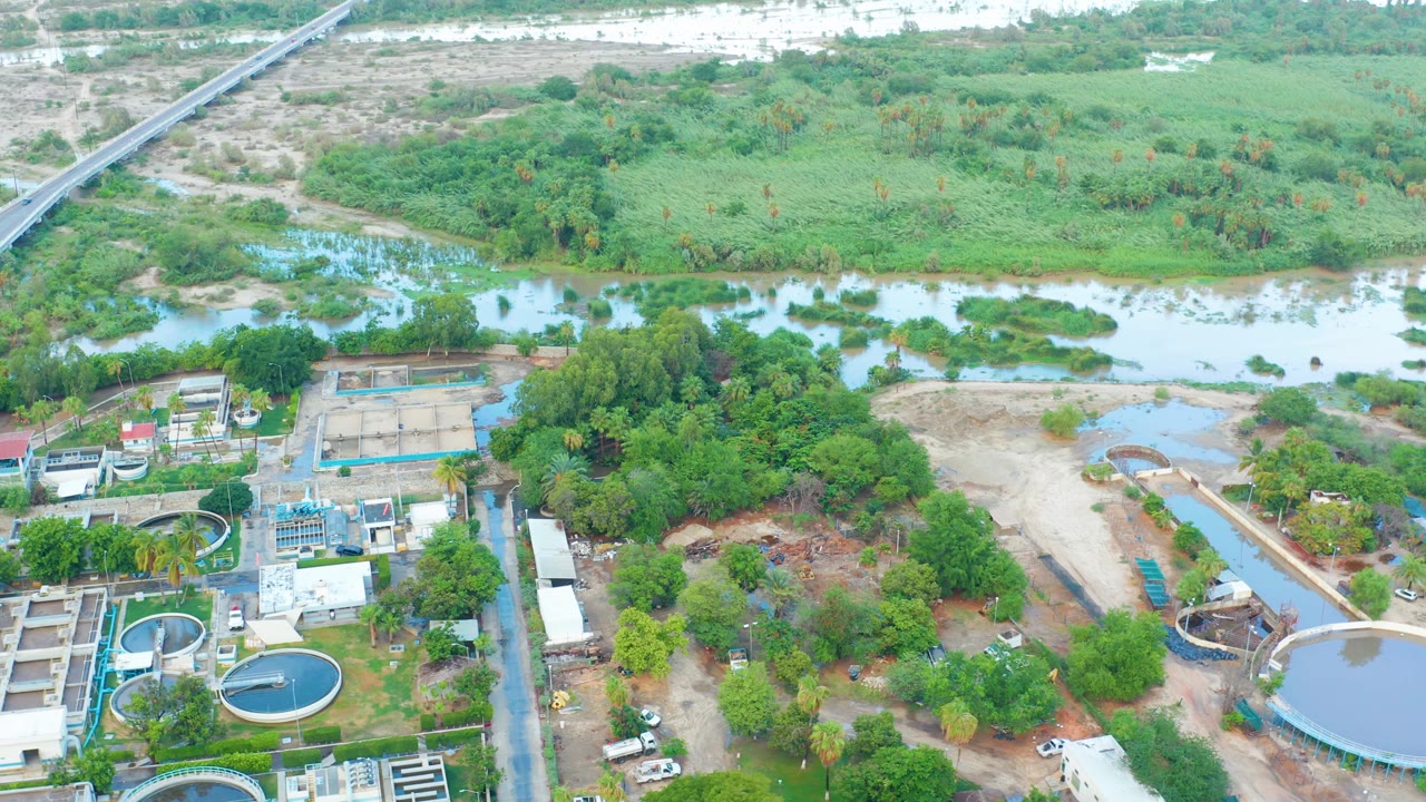 San Jose del Cabo aerial view with round blue water tanks at lower left, rectangular treatment basins, a tree-covered strip, shallow water, and no visible people.