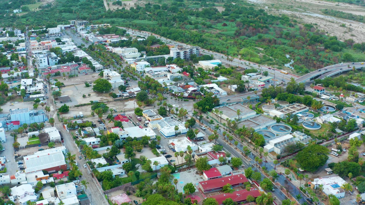 Aerial view over low buildings, streets, trees, and hillside vegetation.