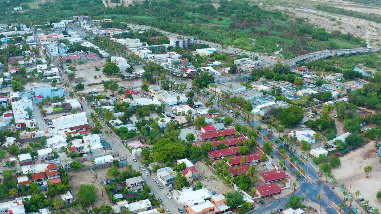 Suburban aerial with red-roofed homes, white buildings, streets, trees, and a dry wash behind them.