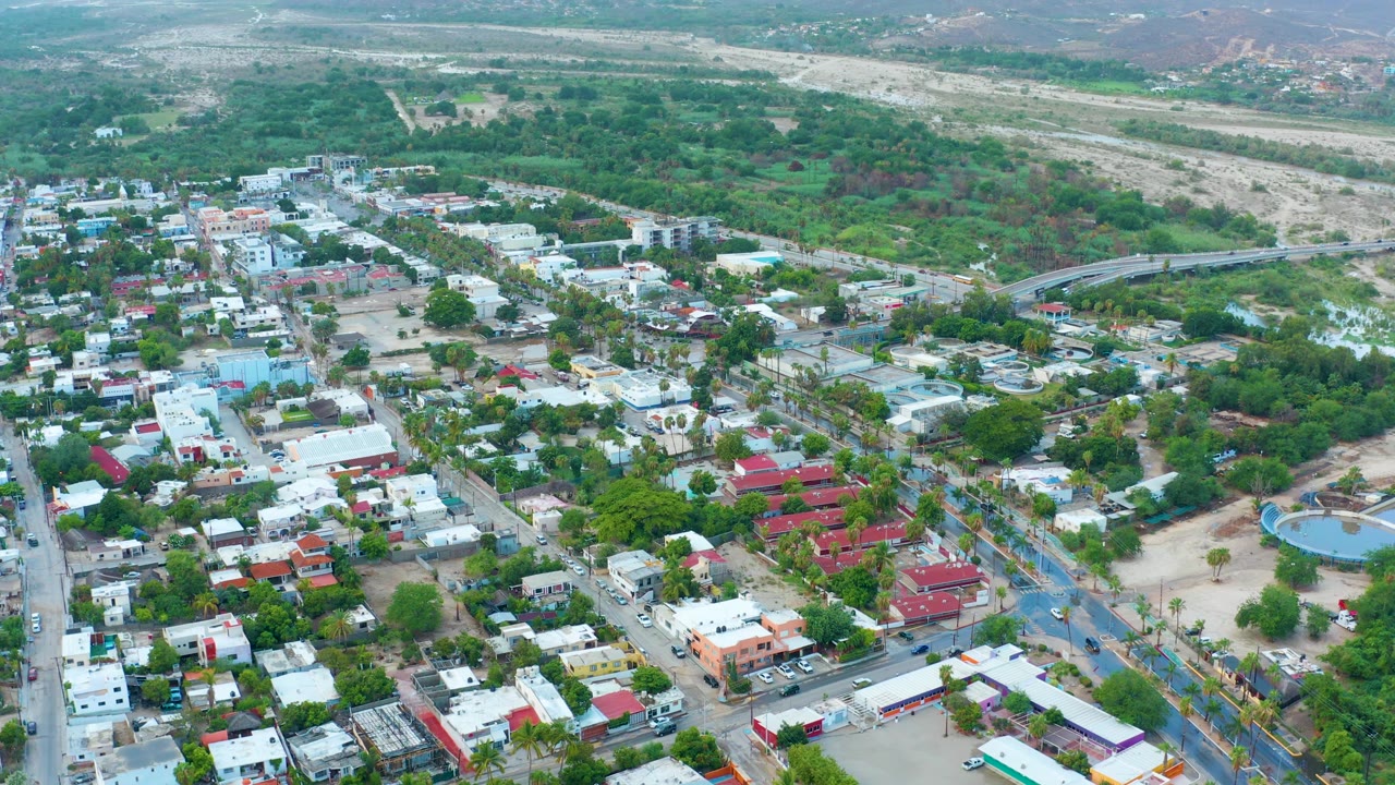 High view of buildings and streets with greenery and dry riverbed behind.