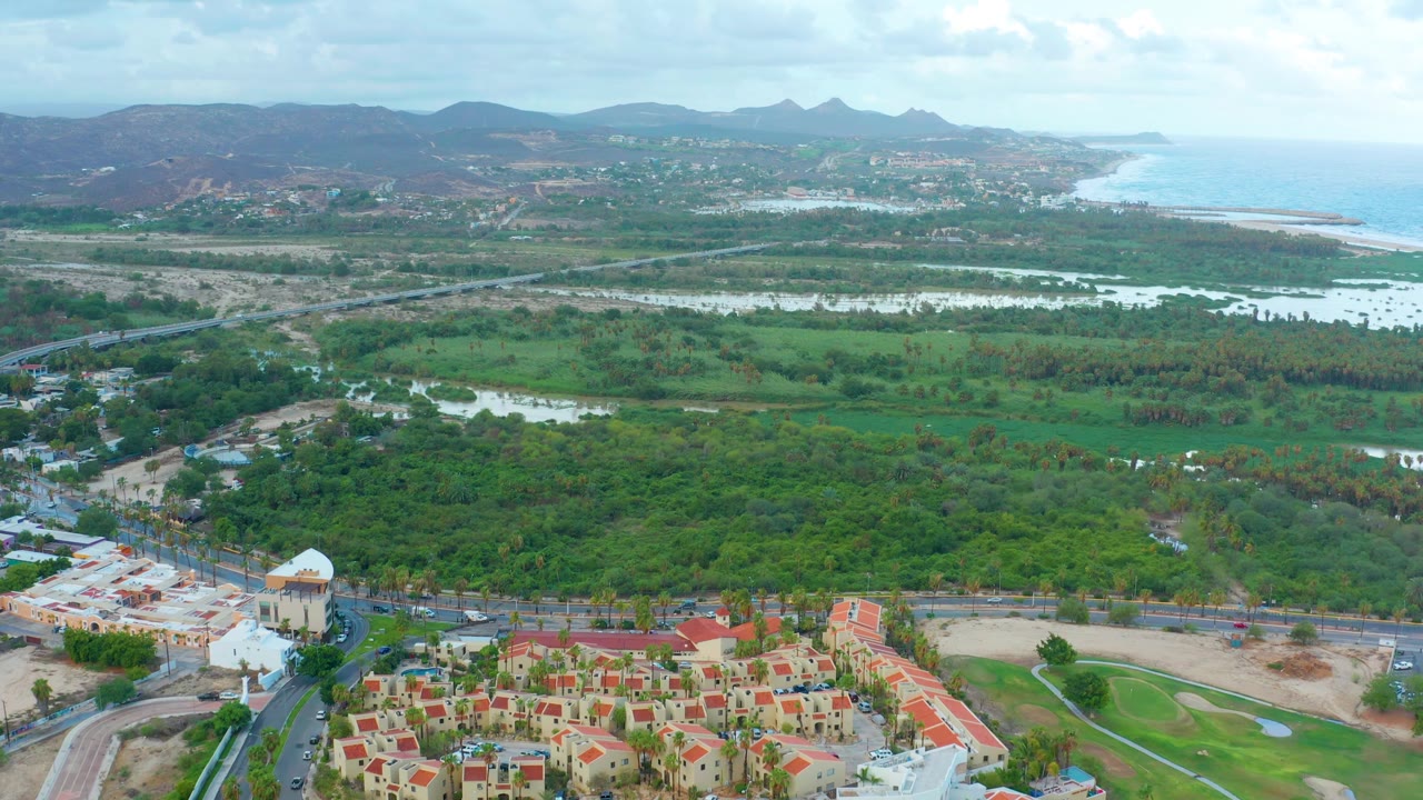 Aerial landscape with housing at the bottom, green vegetation, water, hills, and coastline.