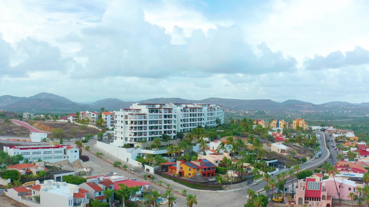 Drone view of apartments, houses, roads, palms, and distant hills.