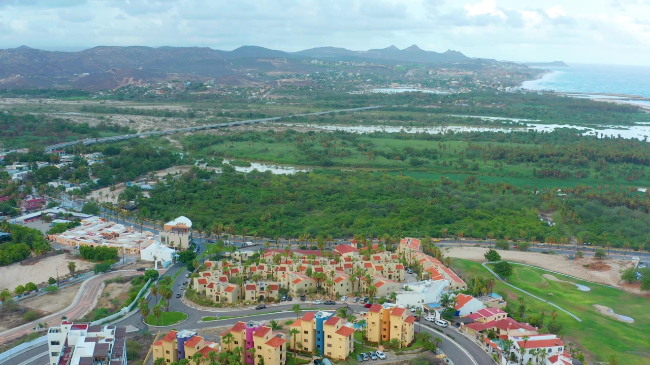 Aerial view with a domed building, housing clusters, roads, fields, water, and mountains.