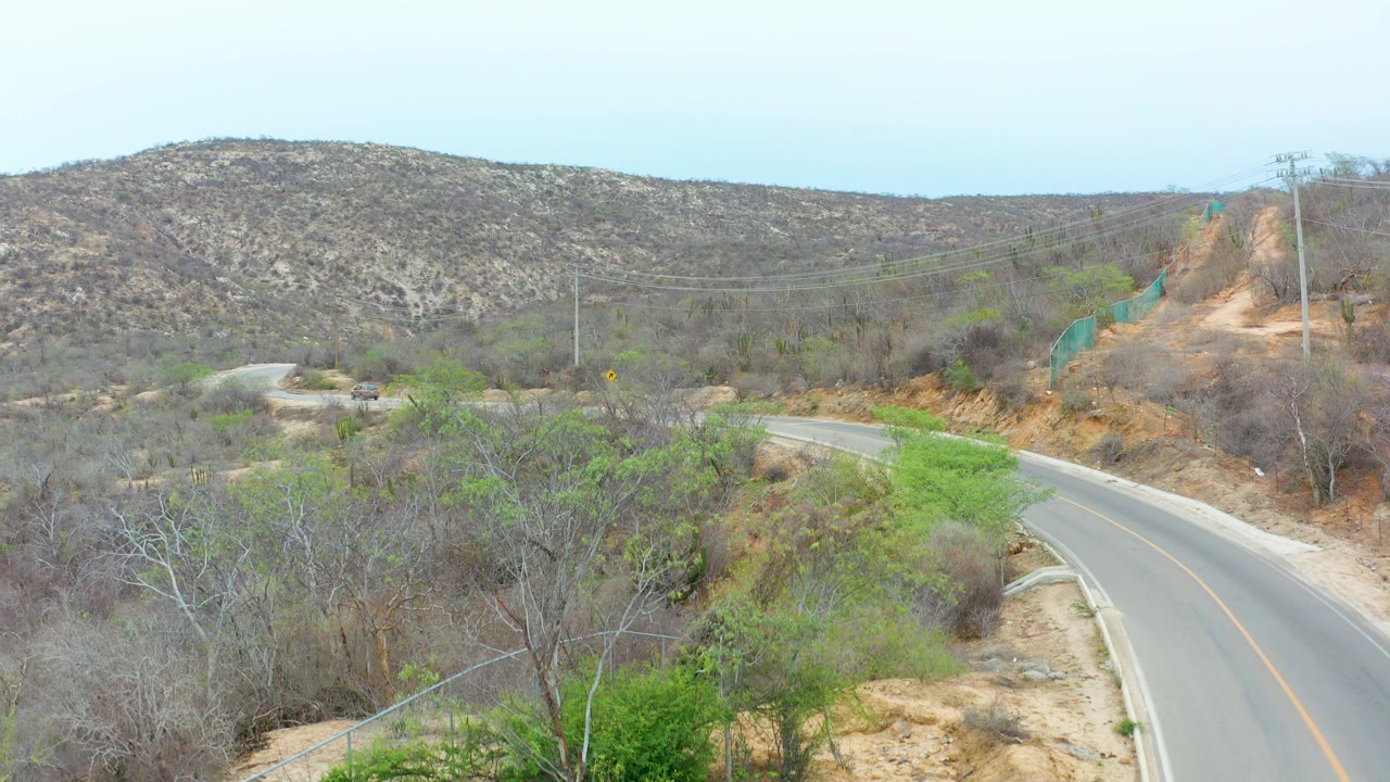 Winding road through dry hills with sparse trees and shrubs.