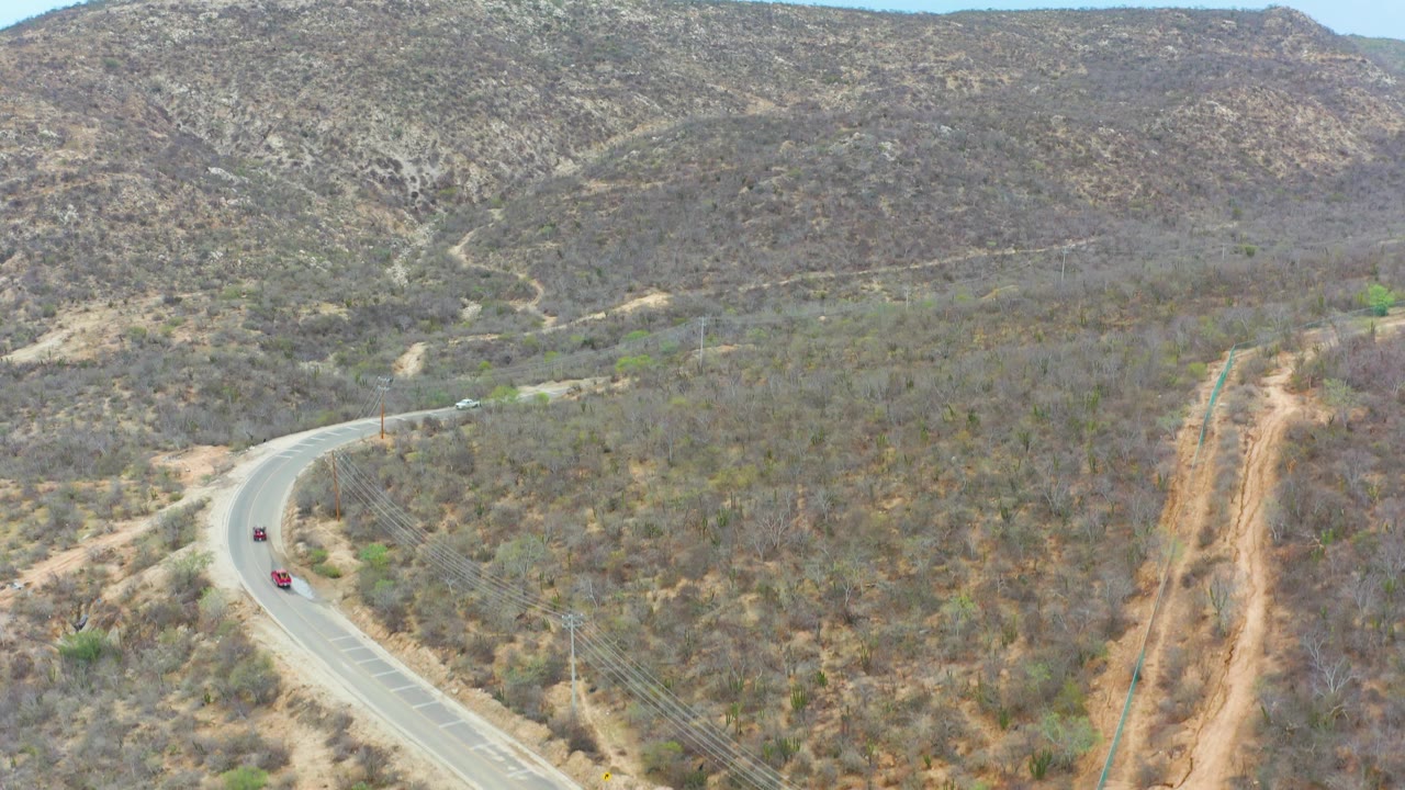 Winding road below dry scrub hills with cars