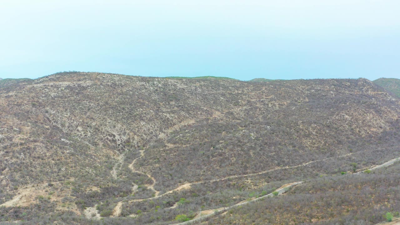 Dry hills with a winding road under a pale blue sky.