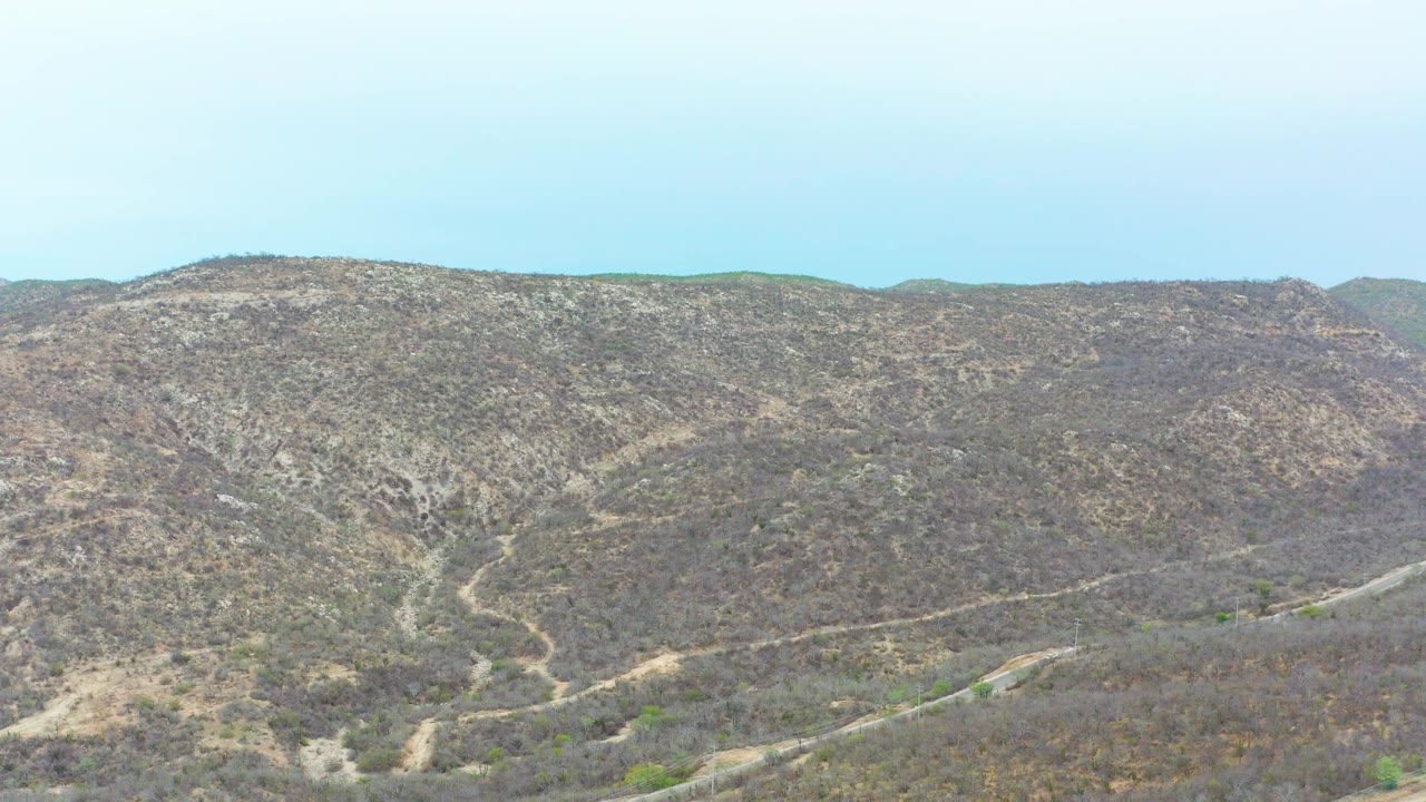 La Playita Los Cabos hillside view with the winding road more centered across the dry brown terrain and no visible people.