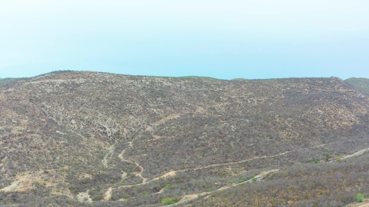 La Playita Los Cabos dry hillside terrain with a curving road running along the lower frame and no visible people.