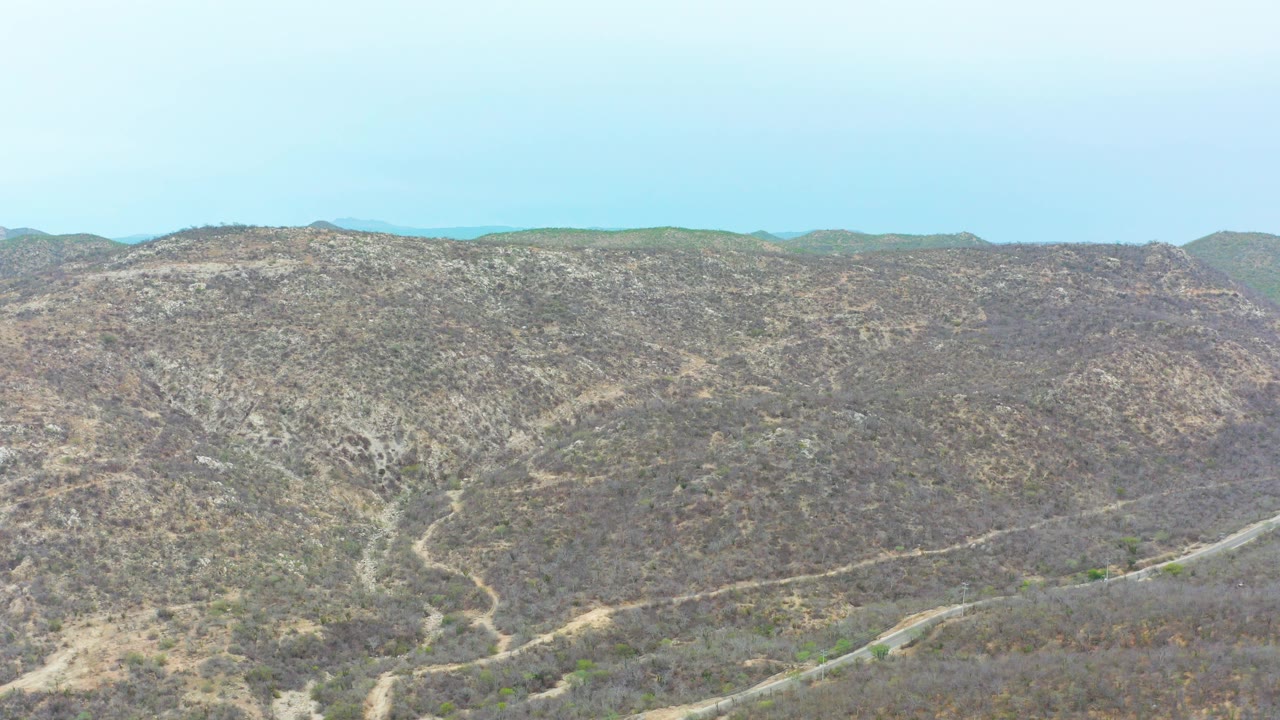 Aerial view of dry hills with winding dirt paths under blue sky.