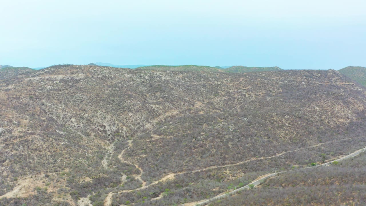 A slightly advanced view of La Playita Los Cabos hills shows branching dirt tracks across brown scrub slopes, distant green ridges, and no visible people.
