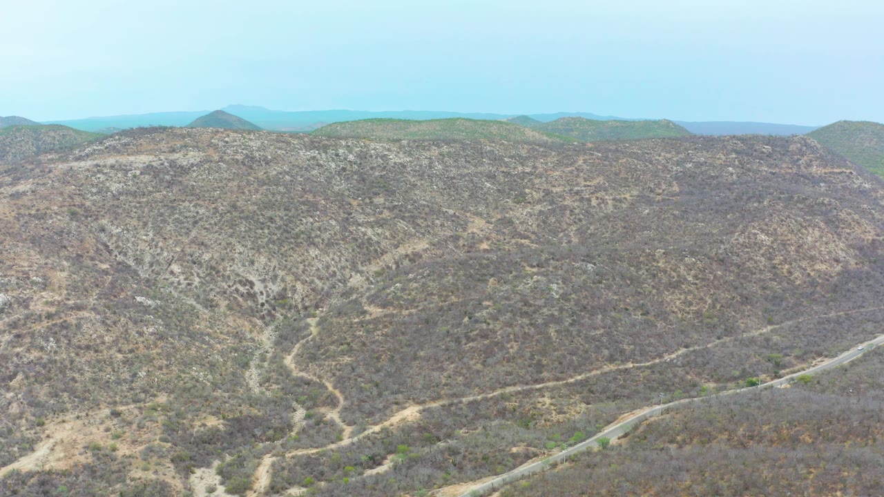 Aerial frame over dry La Playita Los Cabos hills where branching dirt tracks cross scrub-covered slopes, with no visible people.