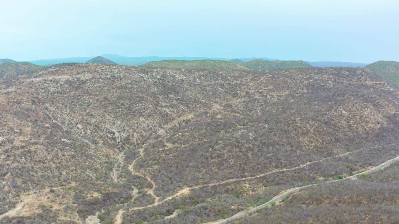 Elevated view of sparse brown hills in La Playita Los Cabos, with a road near the lower slope, layered ridgelines, and no visible people.