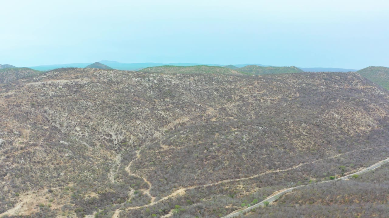Wide La Playita Los Cabos hillside view with pale trails crossing arid scrub, a high horizon, distant mountains, and no visible people.