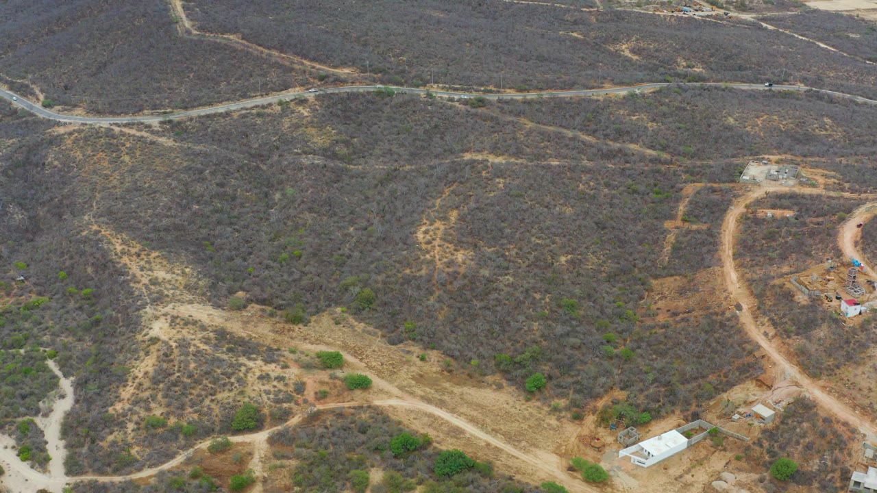 Aerial view in La Playita Los Cabos with a curved dirt road running through scrub-covered hills, small structures near the bottom, and no visible people.