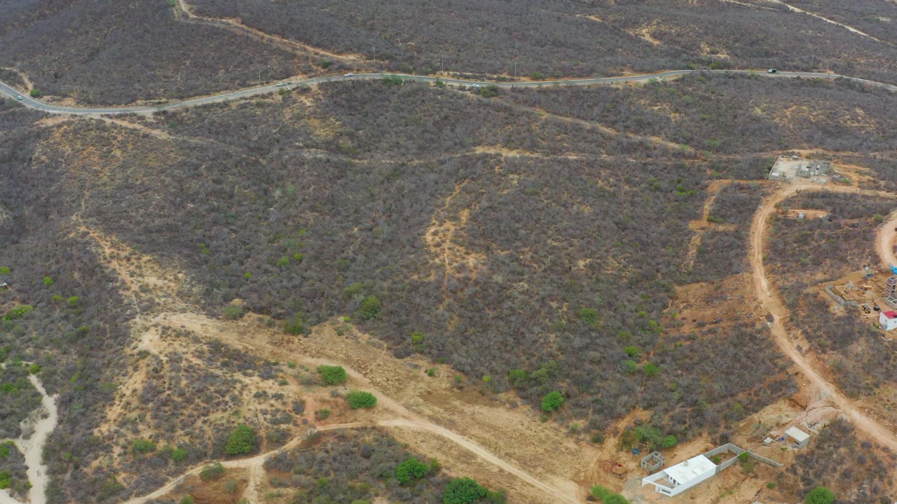 Aerial frame over La Playita Los Cabos with intersecting dirt tracks across dry brown hills, scattered green shrubs, and no visible people.