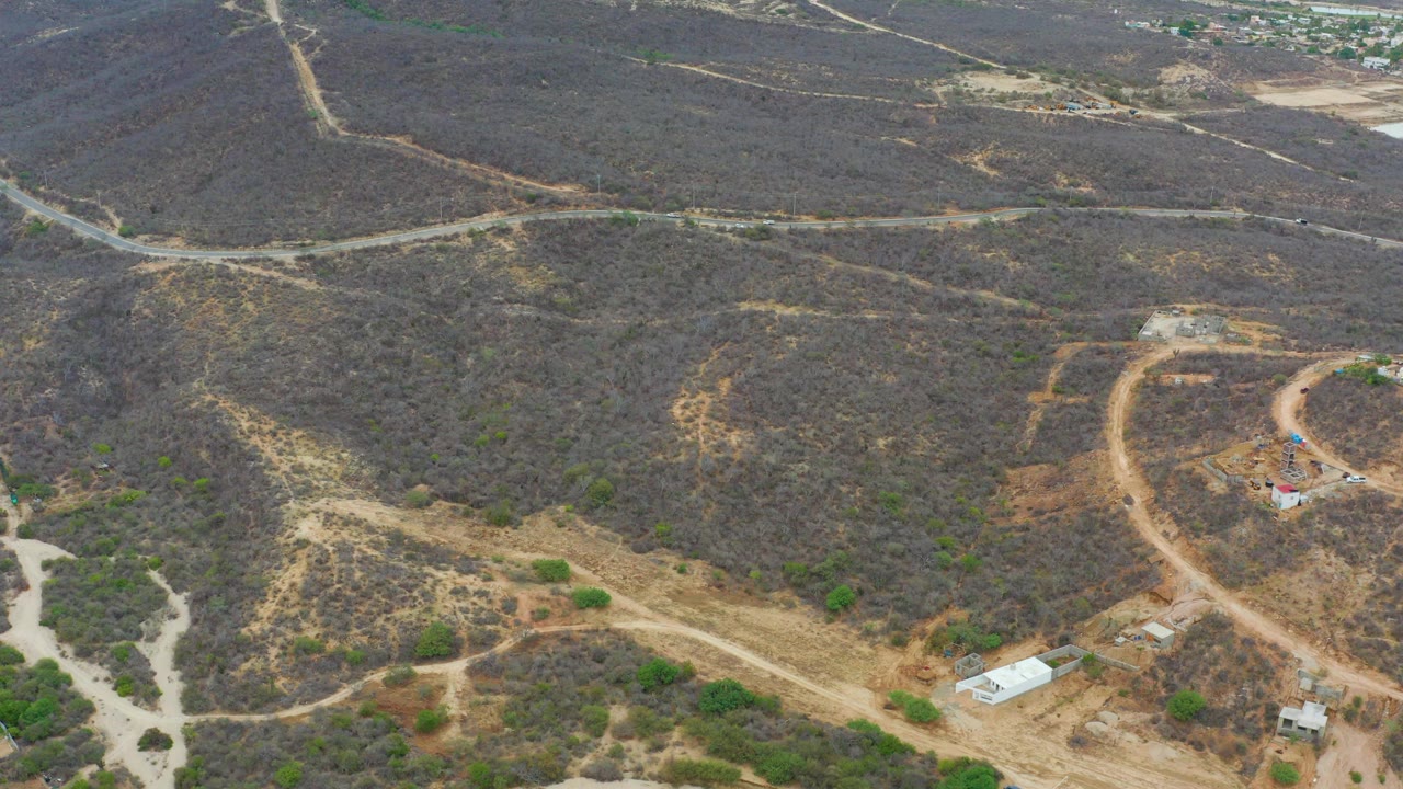 High aerial view of a winding dirt road through scrubby brown hills with small buildings below.