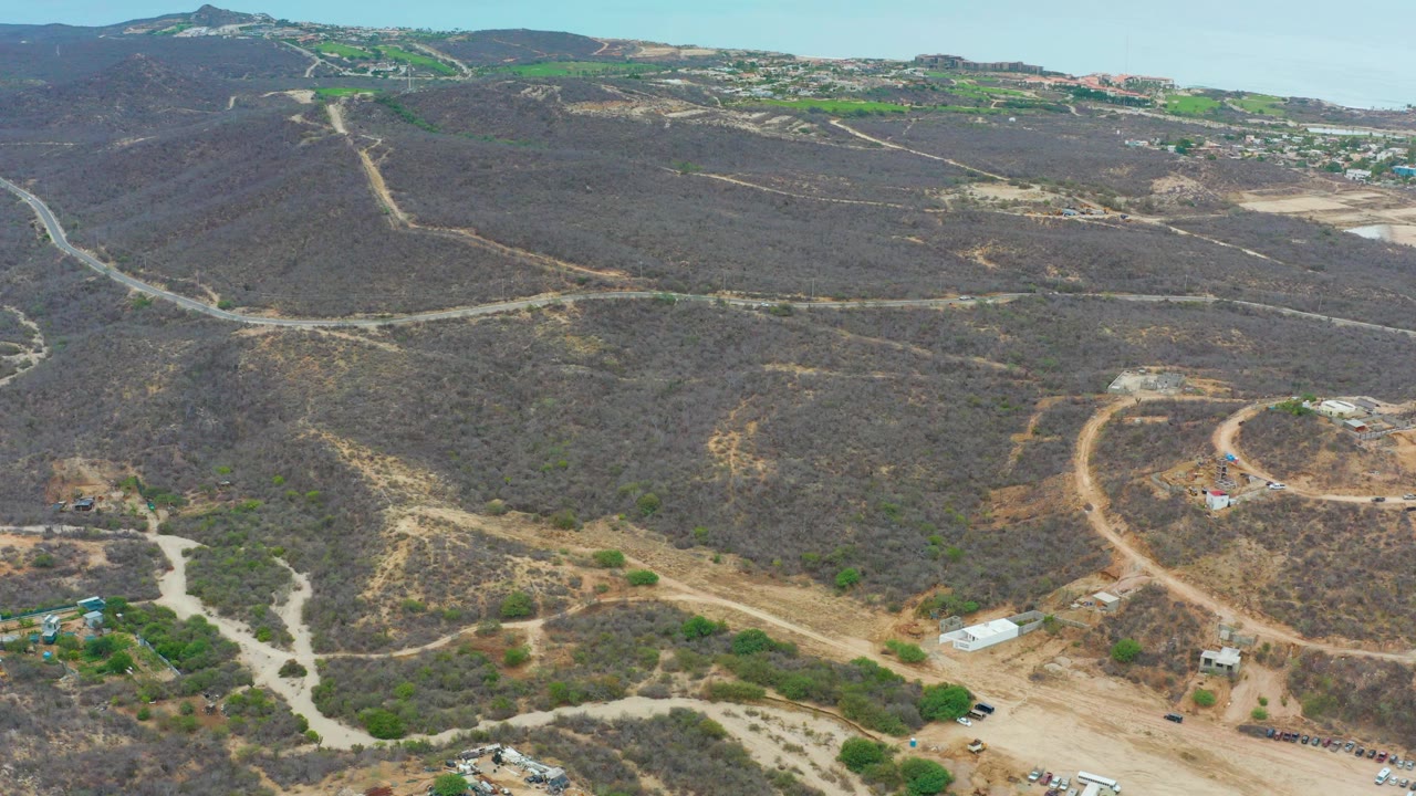 Drone view of winding dirt roads across brown hills with small buildings below.