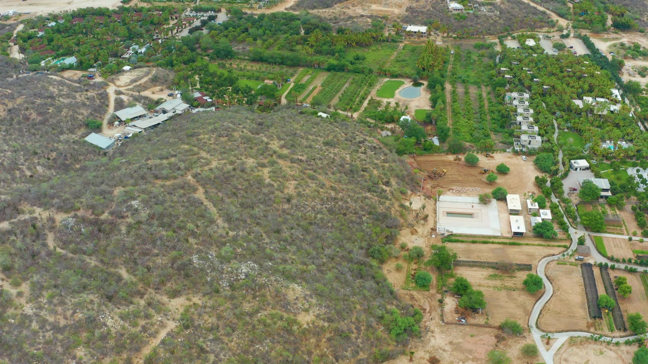 Aerial farmland with a dry hill, curving road, and scattered buildings.