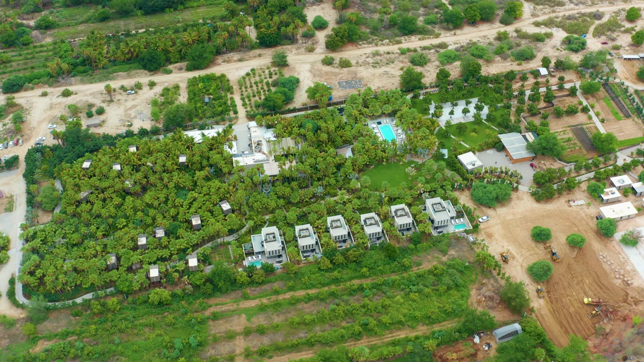 Aerial shot of homes in trees next to a sandy road and construction area.